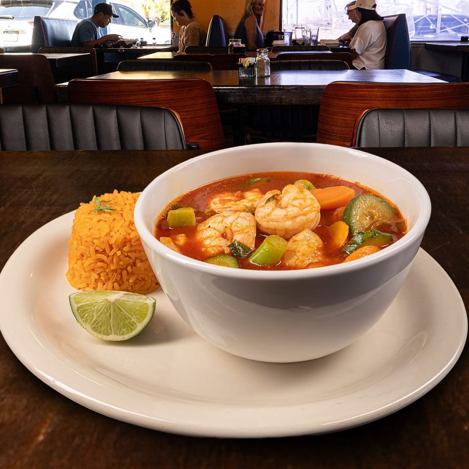 Shrimp soup with vegetables and rice, garnished with lime, in a restaurant setting.