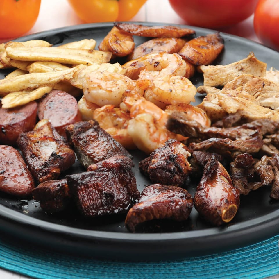 A black platter filled with grilled shrimp, steak, chicken, sausage, and plantains.