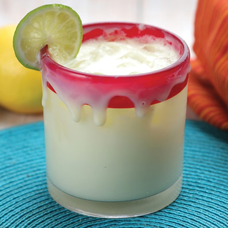 Creamy white drink in a red-rimmed glass with a lime wedge, on a blue placemat.
