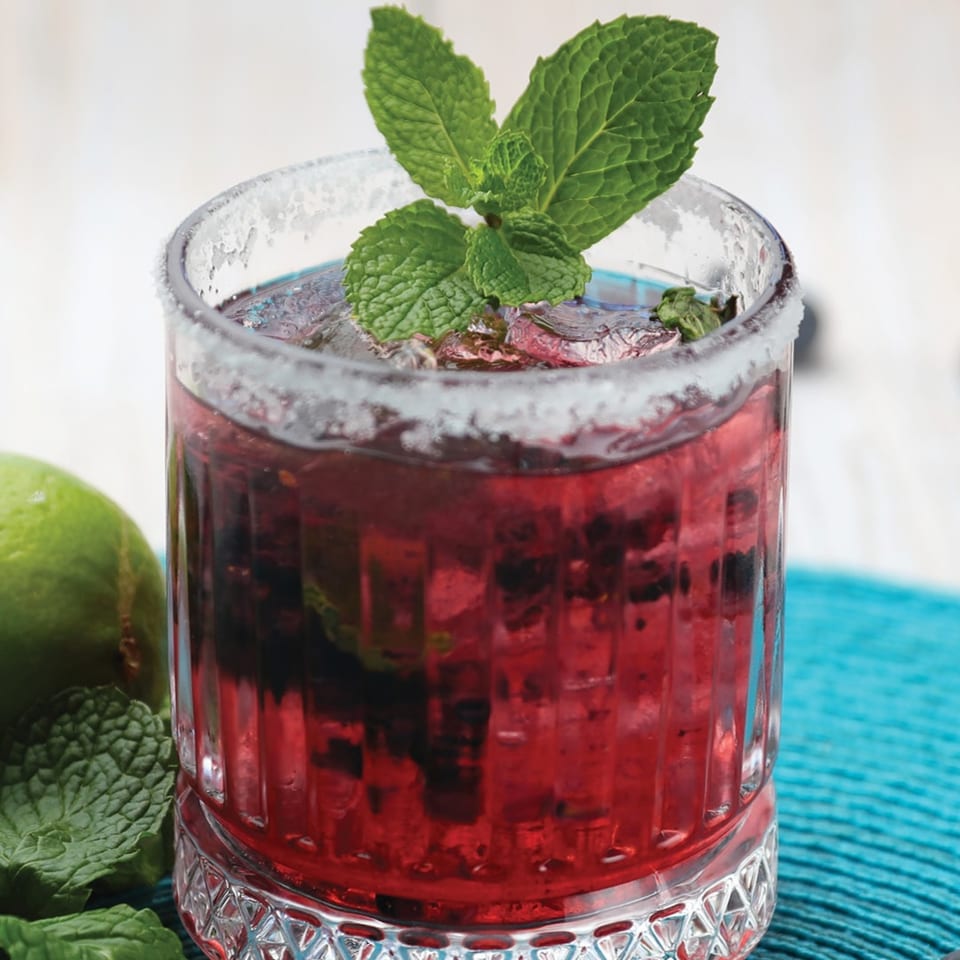 A vibrant red berry margarita with a salted rim, garnished with fresh mint and lime.