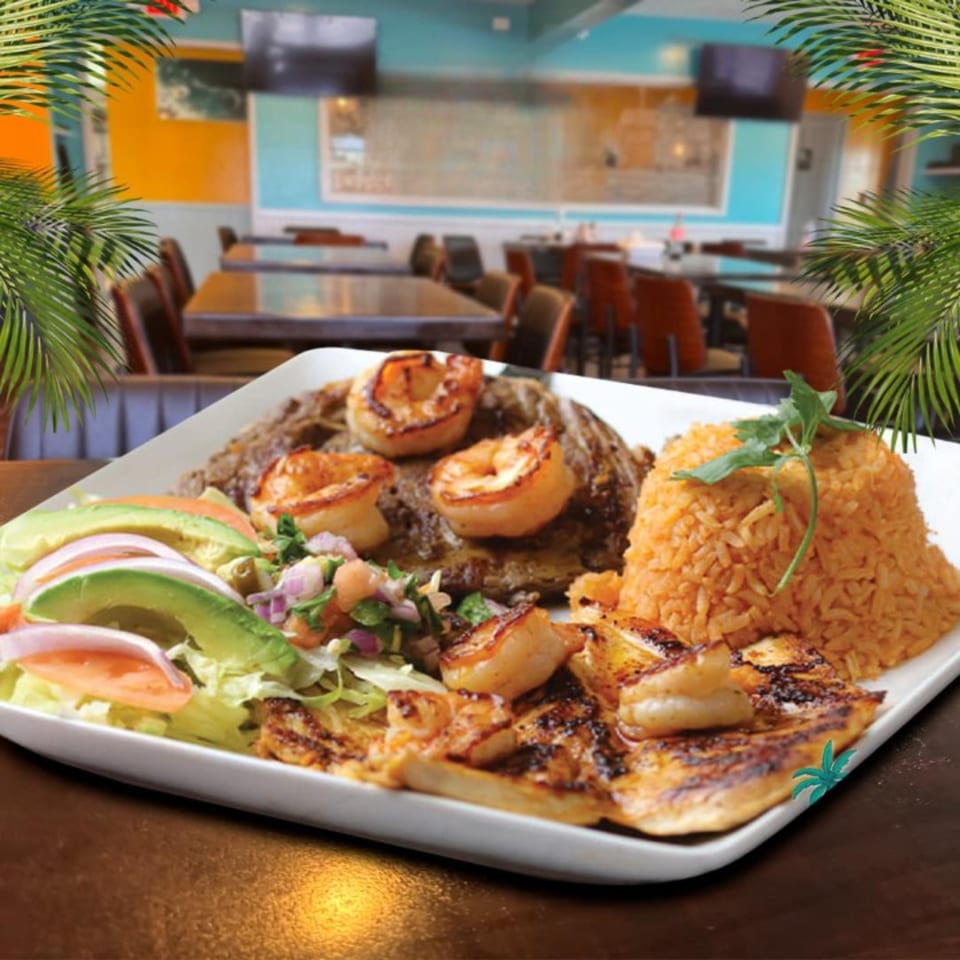 Mexican grilled steak and chicken with shrimp, rice, and salad, in a restaurant setting.