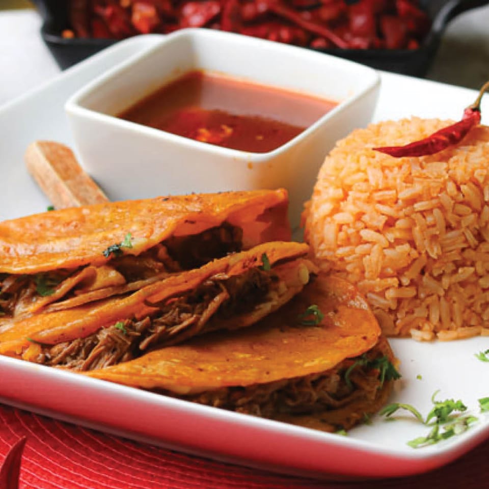 Two Cantina Del Mar birria tacos with a side of red rice and a small bowl of consommé.