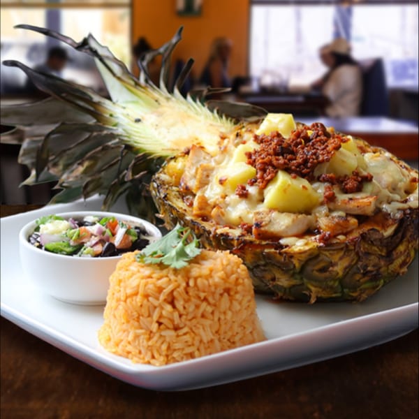 Grilled pineapple stuffed with chicken, cheese, and chorizo, served with rice and black bean salad.
