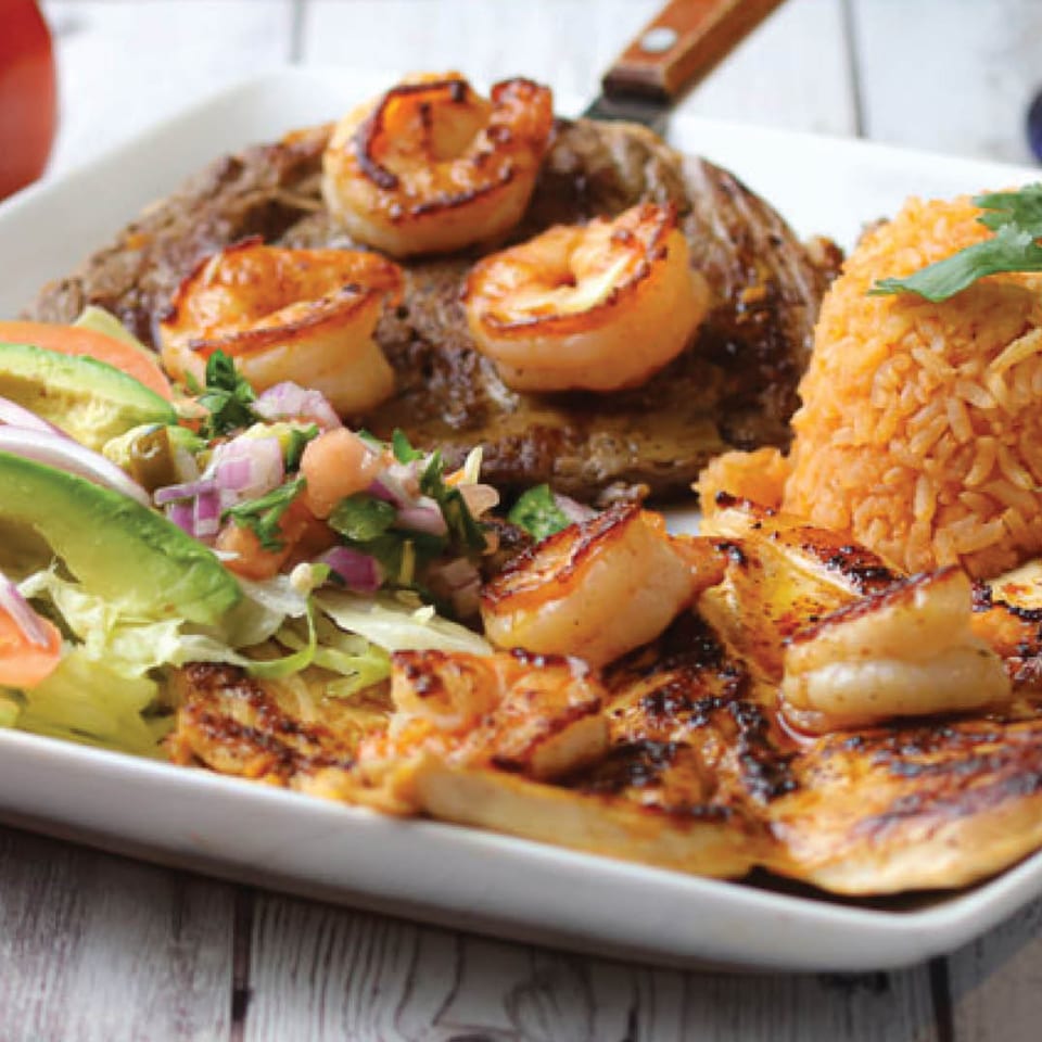 Grilled steak and chicken with shrimp, rice, avocado, and pico de gallo on a white plate.