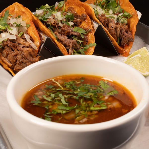 Three Cantina Del Mar birria tacos with cilantro and onions, served with a side of consommé and lime.